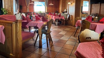 Ein gemütliches Restaurant mit Holzverkleidung und roten Karotischdecken. Die Tische sind für Gäste gedeckt und es herrscht eine einladende Atmosphäre.