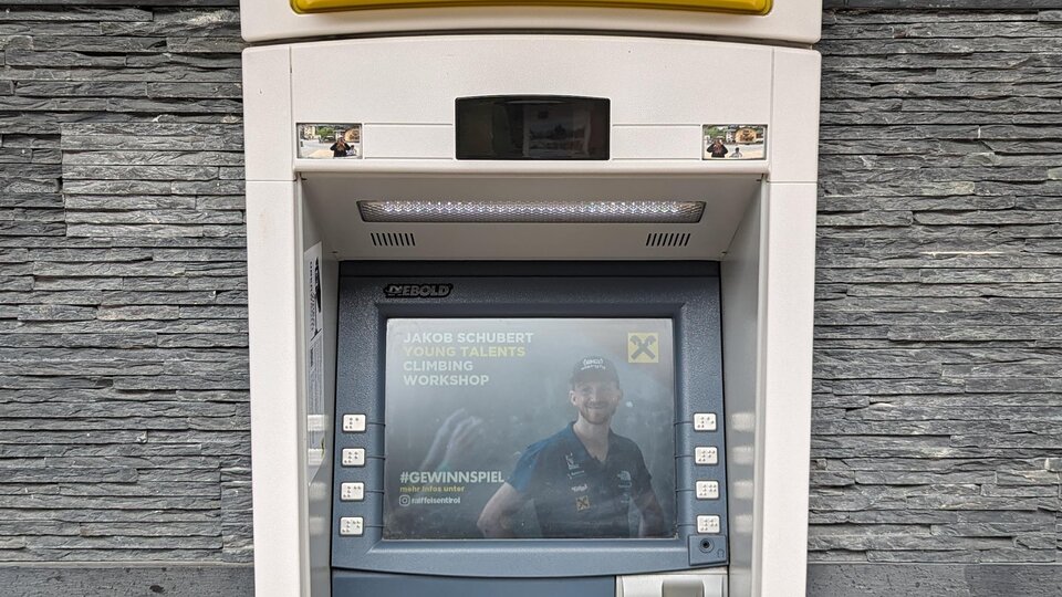 Ein Geldautomat an einer Wand. Er zeigt eine einfache Benutzeroberfläche mit einer Karte und einem Bildschirm.