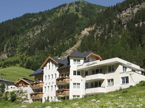 Ein modernes Gebäude in den Bergen. Im Hintergrund sind grüne Hänge und Bäume zu sehen.