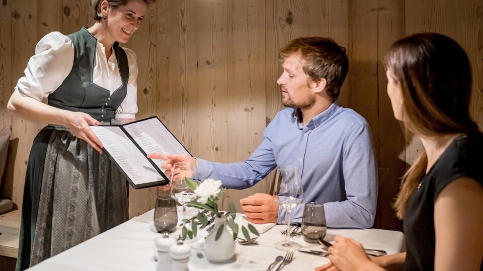 Eine Kellnerin serviert das Menü an ein Paar in einem gemütlichen Restaurant. Die warmen Holzwände schaffen eine einladende Atmosphäre.