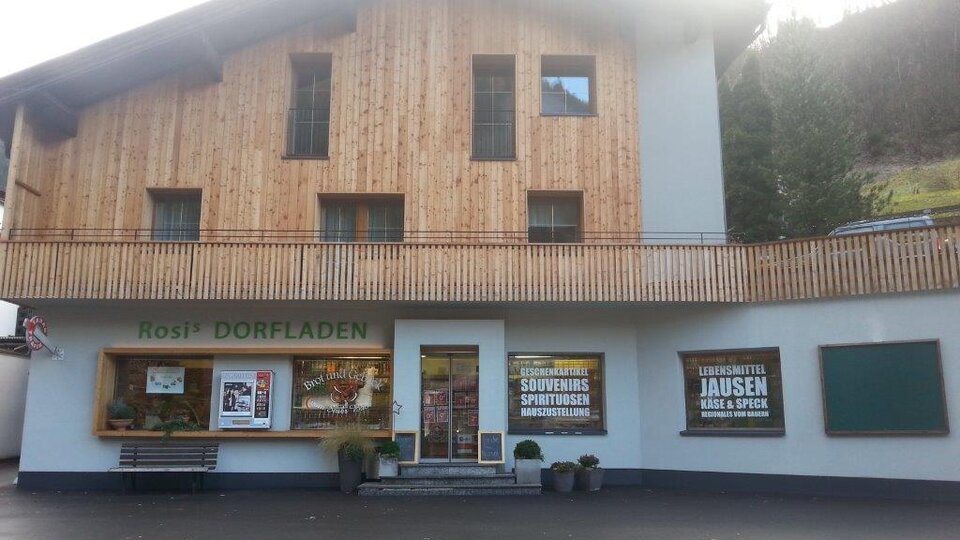 A traditional village shop with a wooden facade and an inviting entrance front. In front of the shop are advertising posters for local products and specialties.