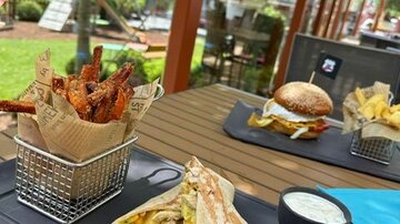 An outdoor table with various dishes. On display are a wrap, fries, a burger, and crispy chicken wings in a fryer.