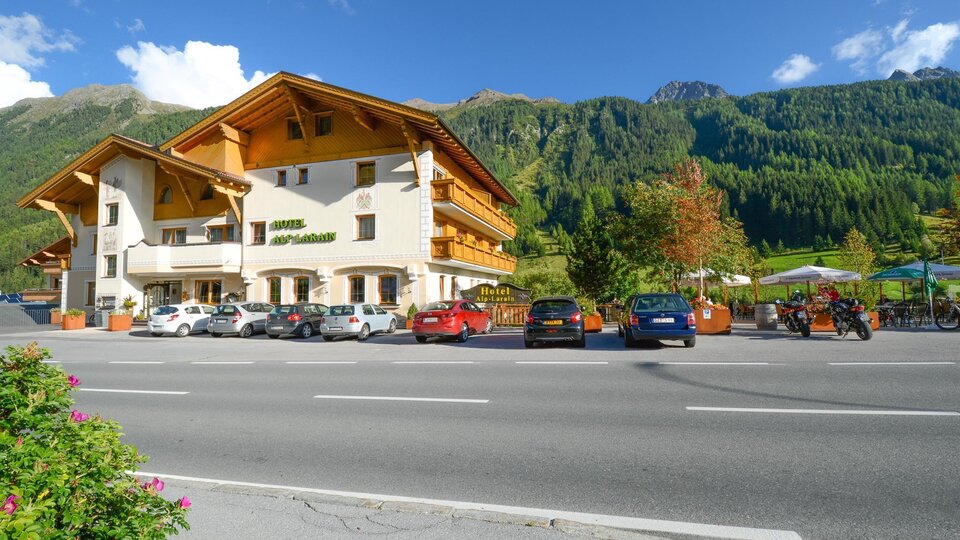 A beautiful hotel with traditional architecture is located by the roadside. In the background, green mountains and trees can be seen.