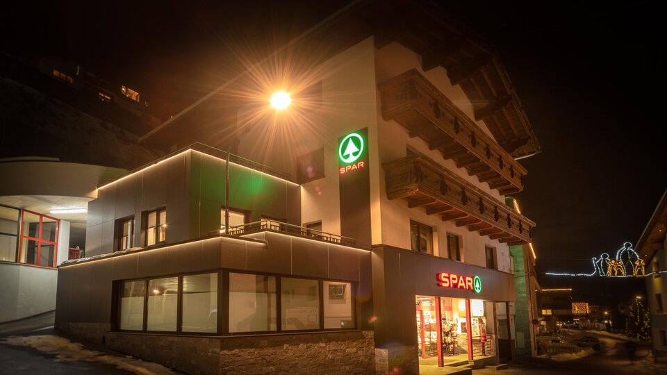 A store with bright lights at night. It is a SPAR market in a modern building.