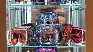 Eine große Auswahl an farbigen Skibrillen in einem Glaskasten. Die Brillen haben verschiedene Designs und spiegelnde Linsen.
