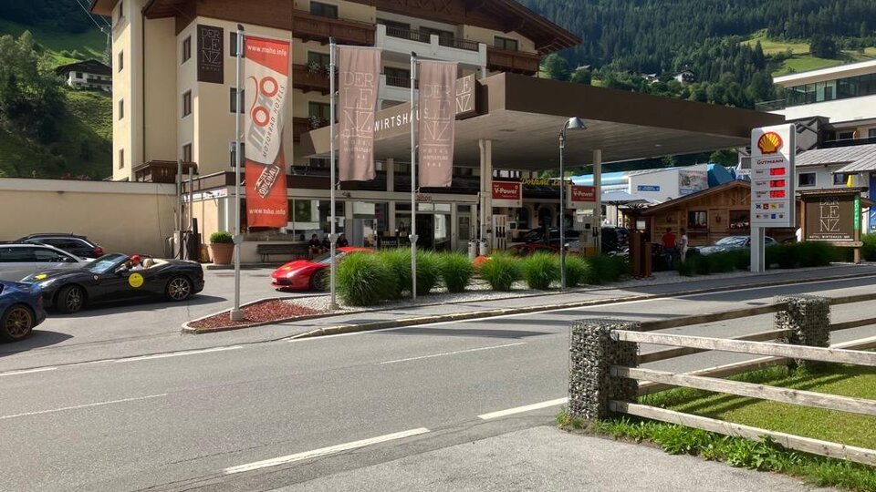 Ein modernes Gebäude mit einem Empfangsbereich und einer Tankstelle im Vordergrund. Umgeben von grünen Hügeln und einer klaren blauen Himmel.