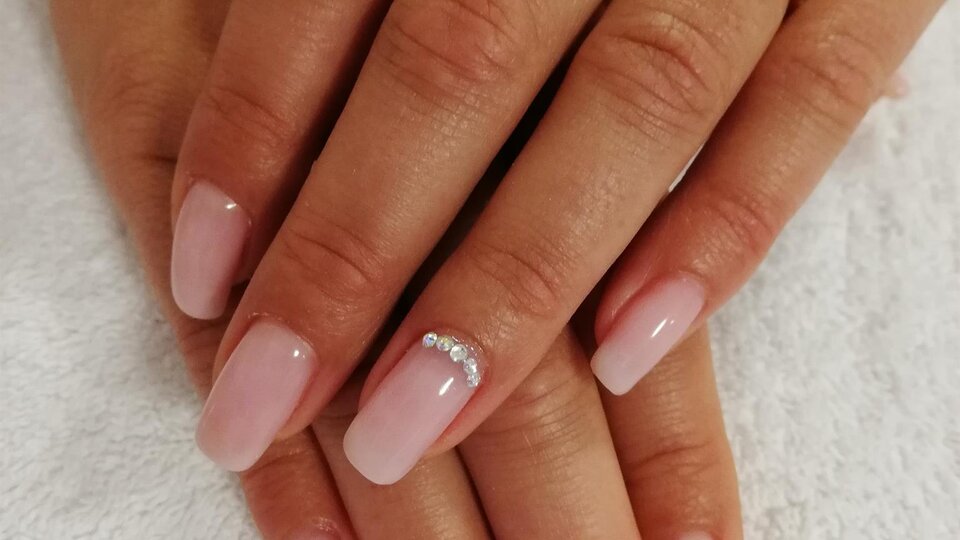 Zwei Hände mit frisch manicurierten, rosa Nägeln liegen auf einem weißen Handtuch. Auf einigen Nägeln sind kleine Schmucksteine.