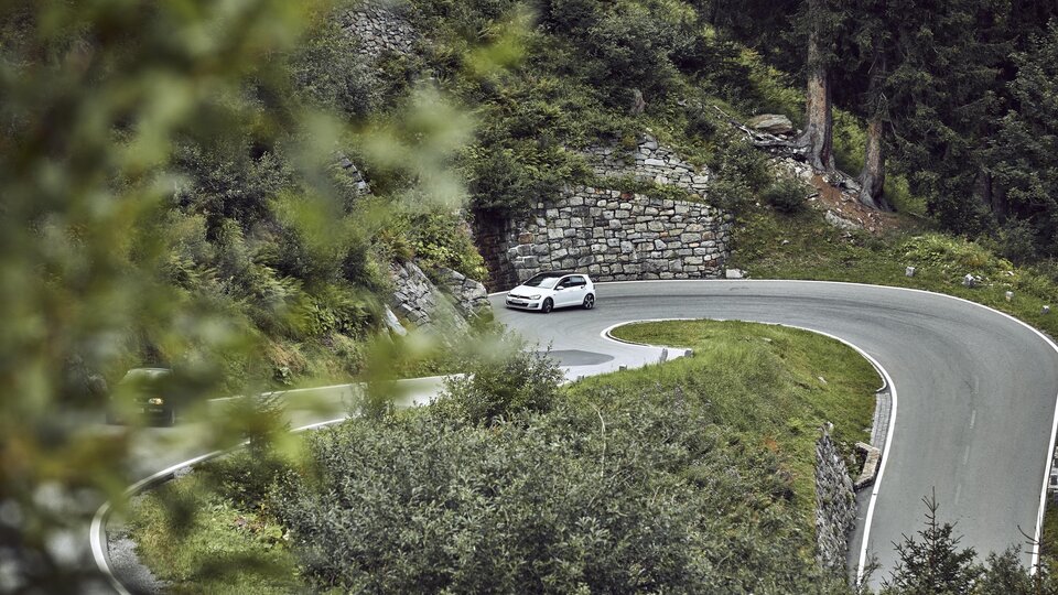 Eine kurvenreiche Straße durch eine grüne Landschaft. Ein Auto fährt um eine scharfe Kurve.