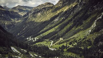 Eine malerische Berglandschaft mit sanften Hügeln und tiefen Tälern. Die kurvenreiche Straße schlängelt sich durch die grüne Vegetation.