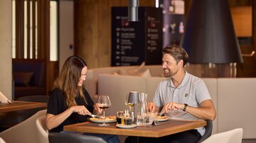 A couple enjoys a romantic dinner in a modern restaurant. They are sitting at a table with drinks and food.