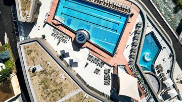 A beautiful swimming pool with loungers and umbrellas. In the background, there is a relaxing spa.