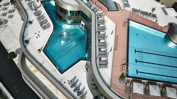 A modern hotel with two swimming pools and numerous loungers. The architecture is elegant and inviting.