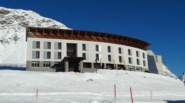 A modern hotel in the mountains, surrounded by snow. The clear blue sky creates a picturesque atmosphere.