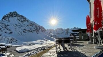 A sunny terrace with a view of snow-covered mountains. In the foreground are chairs and tables inviting relaxation.
