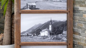 Ein Holzrahmen mit drei Schwarz-Weiß-Fotografien von Landschaften und einer Kirche. Im Hintergrund sind Berge und ein ruhiger See zu sehen. | © Simone Drexel Photography