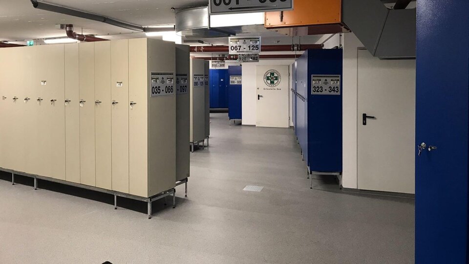 Ein moderner Umkleidebereich mit zahlreichen Schließfächern. Die Wände sind blau gestrichen und die Beleuchtung ist hell.