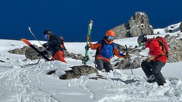 Three skiers ascend through the fresh, white snow. The clear blue sky provides a beautiful contrast to the wintry landscape.