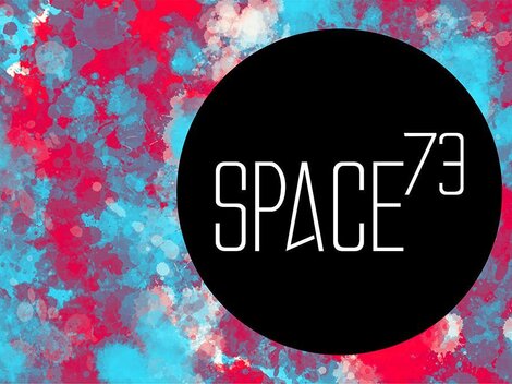 Ein auffälliges, farbenfrohes Hintergrundmuster in Blau und Rot. Das Logo "SPACE73" in der Mitte ist schwarz und modern gestaltet.