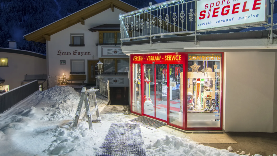 Ein Sportgeschäft mit großen Fenstern, das in einer verschneiten Umgebung bei Dämmerung steht. Das Gebäude hat eine gemütliche Atmosphäre und liegt in den Bergen.