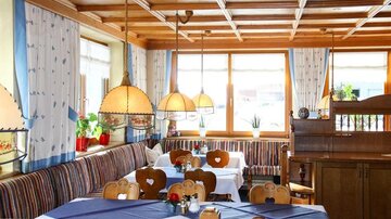 Ein gemütliches Restaurant mit Holzmöbeln und bunten Sitzbänken. Große Fenster lassen viel Licht herein und schaffen eine einladende Atmosphäre.