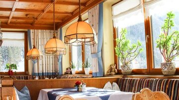 Ein gemütliches Restaurant mit Holzelementen und warmem Licht. Es gibt Pflanzen und dekorierte Tische mit ansprechenden Sitzgelegenheiten.