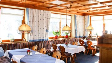 Ein gemütliches Restaurant mit holzverkleideten Wänden und großen Fenstern. Die Tische sind mit blauen Tischdecken dekoriert und die Umgebung wirkt einladend.
