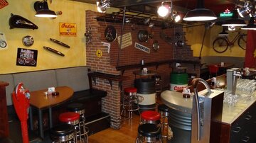 A cozy bar with seating made of metal and wood. The walls are decorated with various motorcycle accessories and nostalgic decorations.