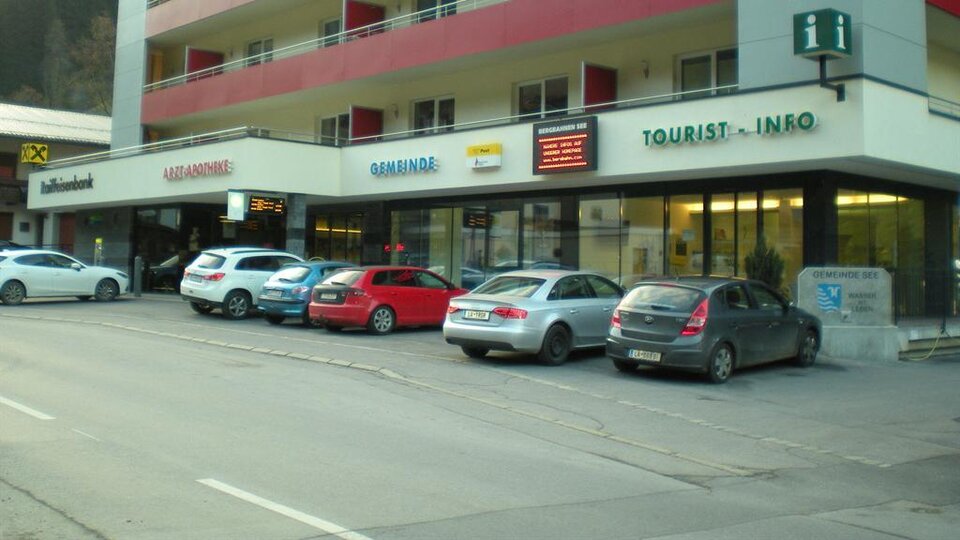 A modern building with several shops and parking spaces. Above, the balconies of the upper floors are visible.