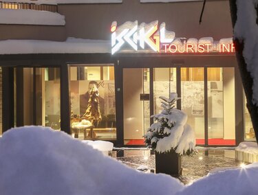 Ein modernes Gebäude mit dem Schild „Tourist Info“ in einer verschneiten Landschaft. Der Eingang ist einladend und zeigt eine winterliche Atmosphäre.