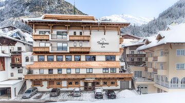 A modern hotel in alpine style, surrounded by snow-covered mountains. The facade features wooden details and large windows.