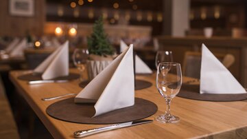 An elegant table in a restaurant, beautifully set with fabric napkins and glasses. In the background, warm light accents and a cozy atmosphere can be seen.