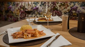 An elegant table setting with a dish of shrimp and side dishes. Two glasses of wine sit nearby, surrounded by a stylish environment.