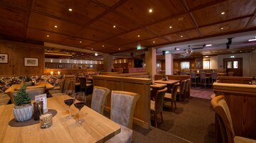 A cozy restaurant with wooden decor and warm lighting. Tables are set and there is an inviting atmosphere.