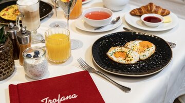 A beautifully set table with a breakfast arrangement. It includes fried eggs, croissants, juices, and yogurt.