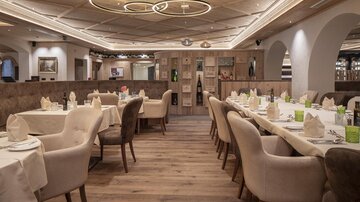 Ein elegantes Restaurant mit modernen Möbeln und sanftem Licht. Die Tische sind schön eingedeckt und laden zum Verweilen ein.