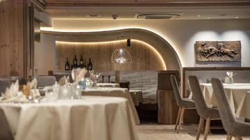 Ein elegantes Restaurant mit Holzelementen und sanftem Licht. Tische sind geschmackvoll gedeckt und eine kunstvolle Wandgestaltung verleiht dem Raum Charakter.
