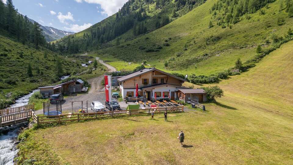 A picturesque landscape with an inn in the mountains. A river and green meadows surround the building.