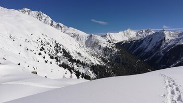 Eine schneebedeckte Berglandschaft mit klaren blauen Himmel. Die Gipfel ragen majestätisch über die verschneiten Täler.