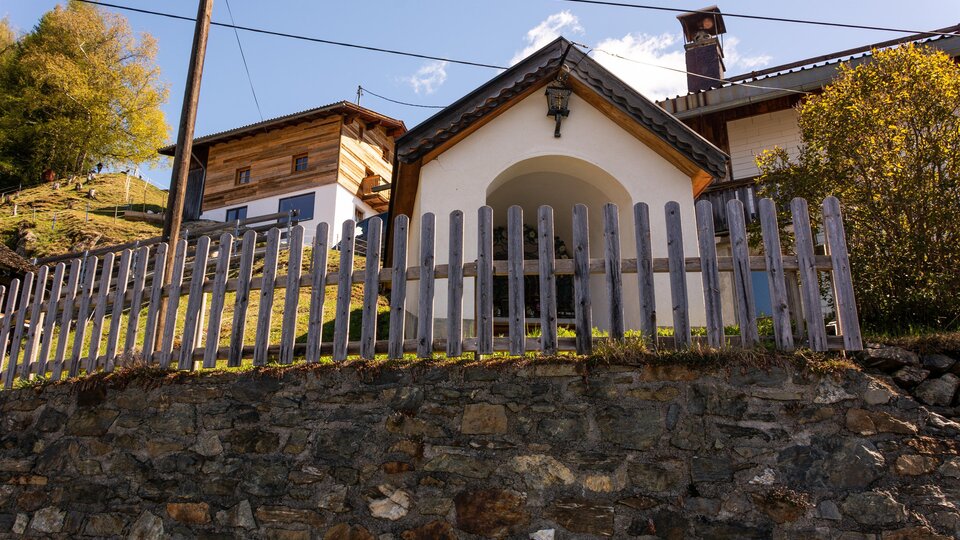 A charming house with a wooden fence and a picturesque location. Surrounded by nature and mountains, it radiates coziness. | © Bernhard Gruber – Photography