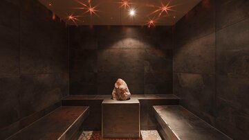 Ein entspannender Wellnessraum mit dunklen Wänden und einer Relaxbank. In der Mitte steht ein Salzstein auf einem Podest.