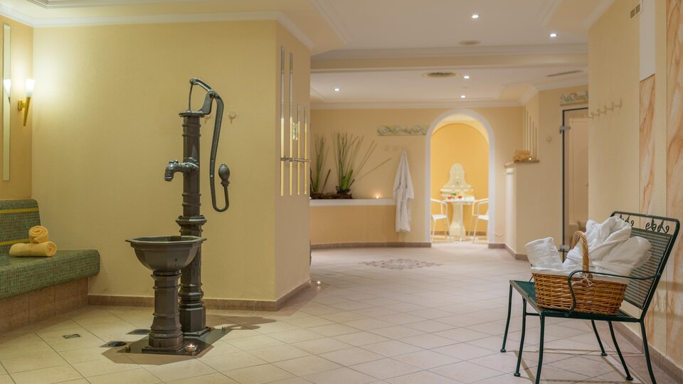 An elegant wellness area with soft colors and cozy furniture. At the center is an antique fountain and a relaxing atmosphere.