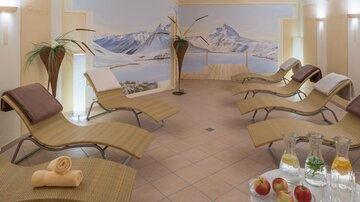 A relaxing wellness area with loungers and soft lighting. In the background, there is a mountain landscape with a calm atmosphere.