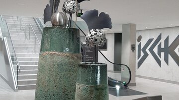 Zwei dekorative Vasen aus Keramik, eine größere und eine kleinere, stehen auf einem Tisch. Sie sind mit stilisierten Blumen und modernen Akzenten verziert.