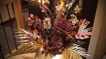 Ein dekorativer Blumenstrauß in einer goldenen Vase. Die Komposition besteht aus roten Rosen und verschiedenen Pflanzen, die eine elegante Atmosphäre schaffen.