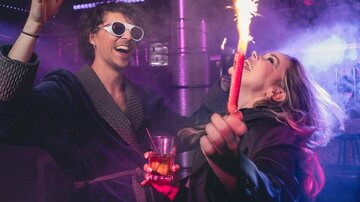 A cheerful party scene with two people playing with glowing sparks. They are having fun while celebrating in a vibrant environment.