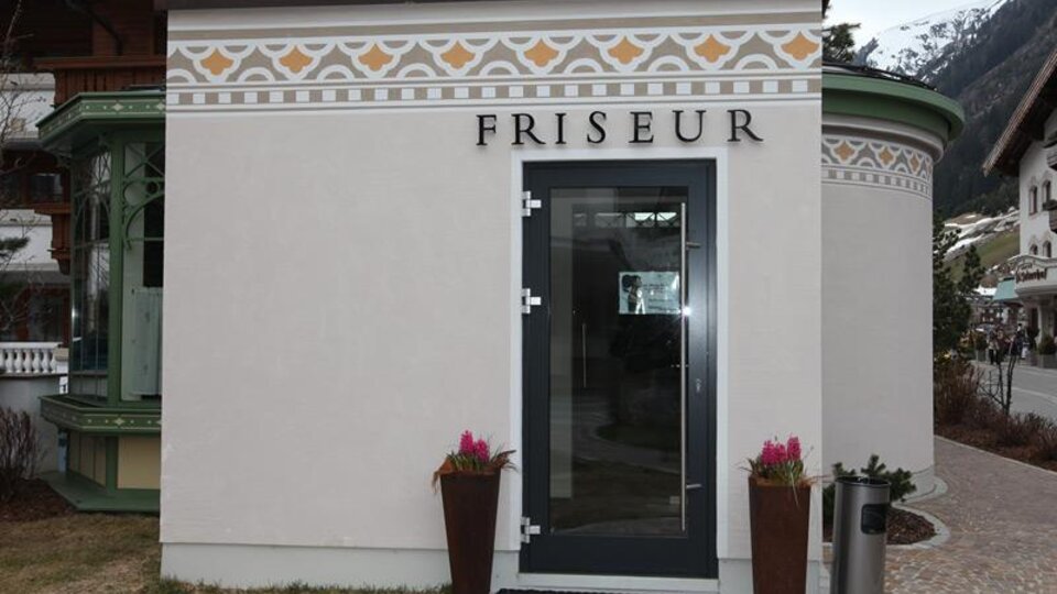 Ein Friseursalon mit einer eleganten Fassade. Die Eingangstür ist modern und es gibt Pflanzen auf beiden Seiten.