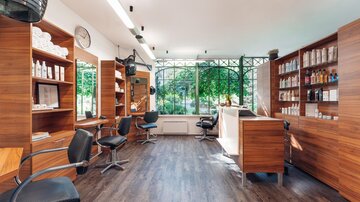 Ein frischer Friseursalon mit modernen Stühlen und Regalen voller Pflegeprodukte. Große Fenster sorgen für viel Tageslicht und Blick ins Grüne. | © Trofana Royal Resort/valentin_fotoo