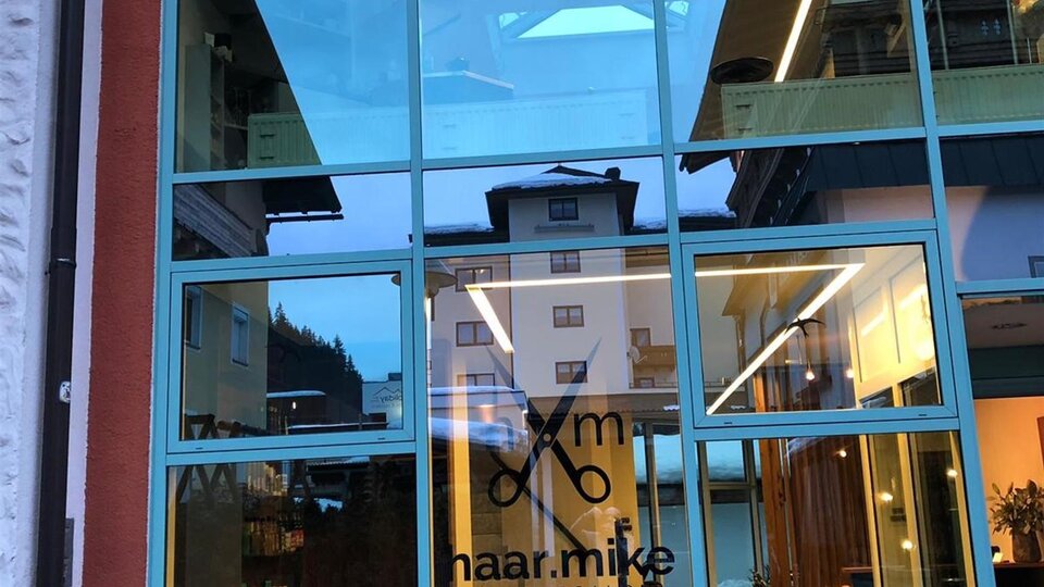 A modern hair salon with large glass windows. The name "naar.mike" is prominently visible on the door.