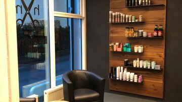 A stylish hair salon with modern chairs and a wooden shelf. The shelf is filled with various hair care products.