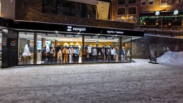 A sports and fashion store with a large shop window front. The ground is covered in snow and it seems to be night.